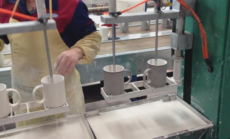 ceramic mug glazing process Ceramic mugs receiving glaze coating during manufacturing.